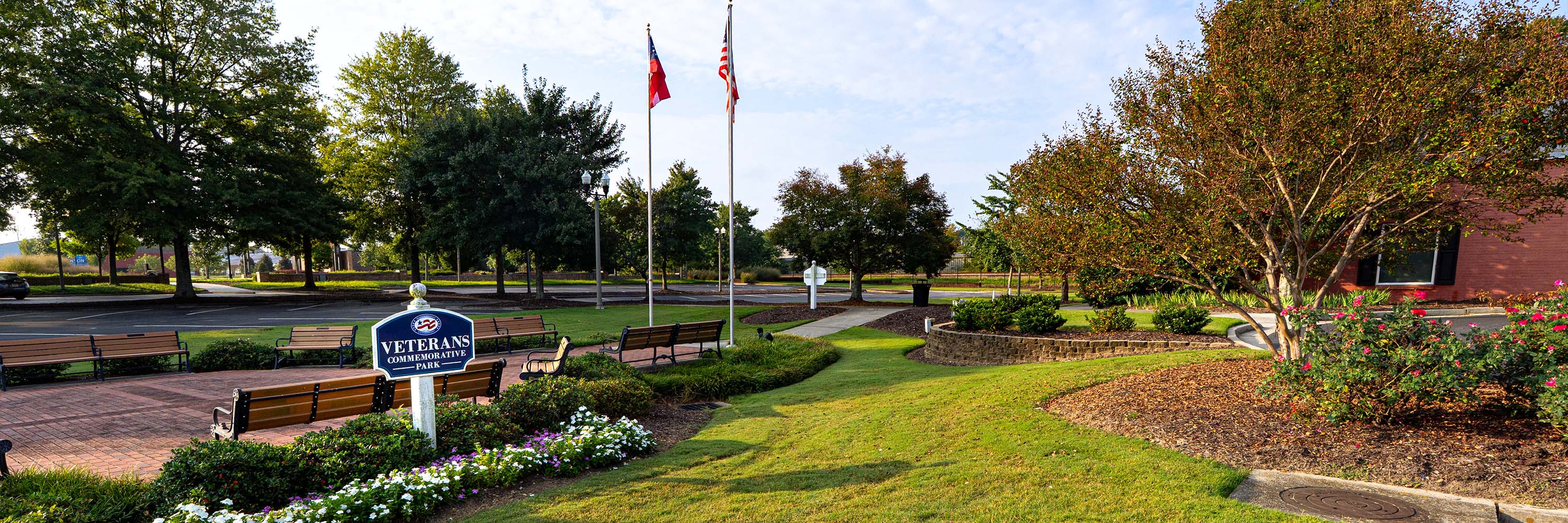 Veterans Park wide image, showing the park sign, flower bed, flags, and side of Community Center in spring